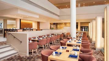 A spacious hotel lobby with multiple seating areas, a staircase, and a reception desk.