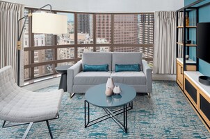Una habitación de hotel moderna con sofá, sillón y una mesa de centro redonda.
