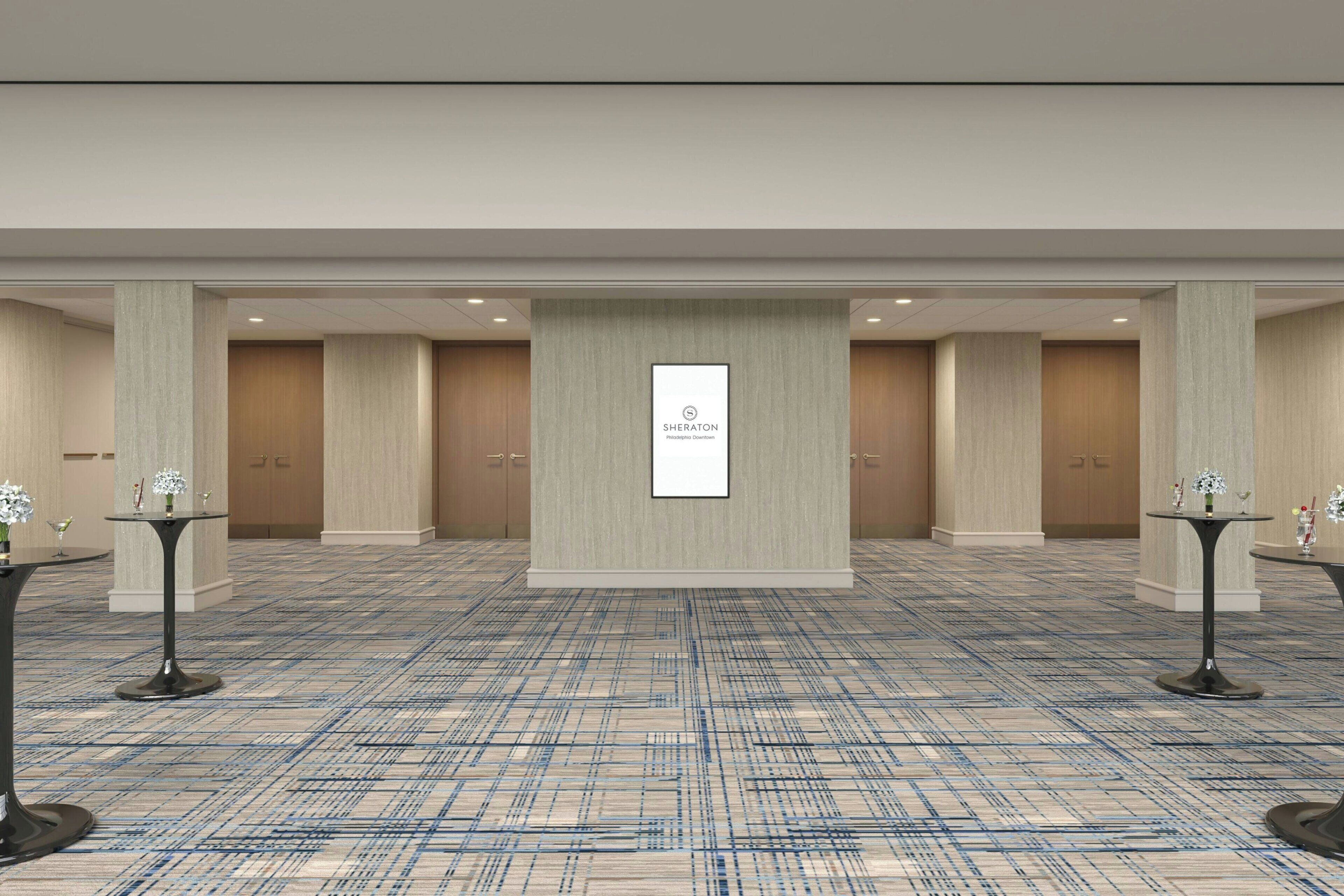 A conference room with a carpeted floor, a central wall-mounted sign, and two tables with floral centerpieces.