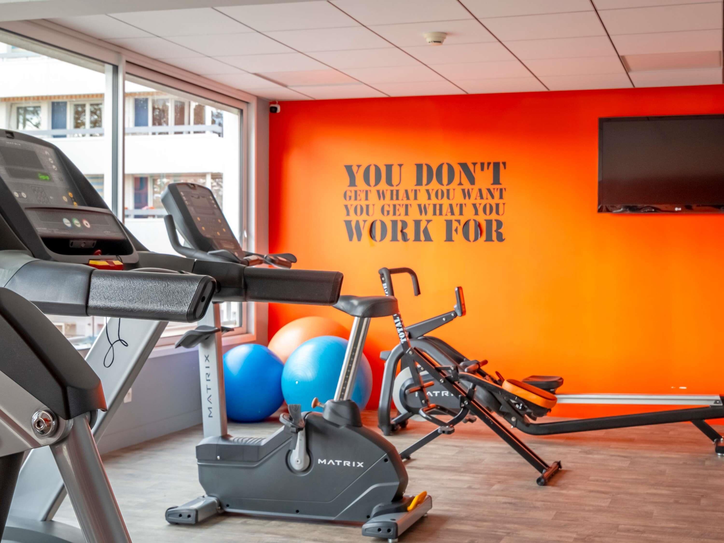 A gym with treadmills, an elliptical, and exercise balls, featuring a motivational quote on the wall.