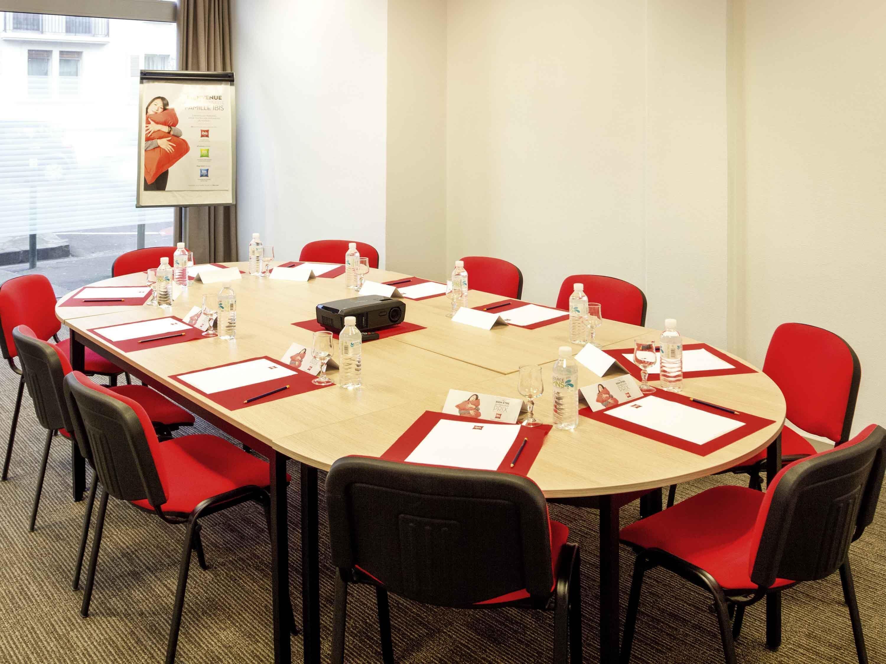 A conference room with a long table, red chairs, name cards, water bottles, and a projector.