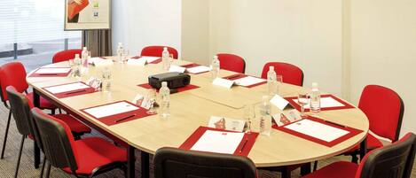 A conference room with a long table, red chairs, name cards, water bottles, and a projector.