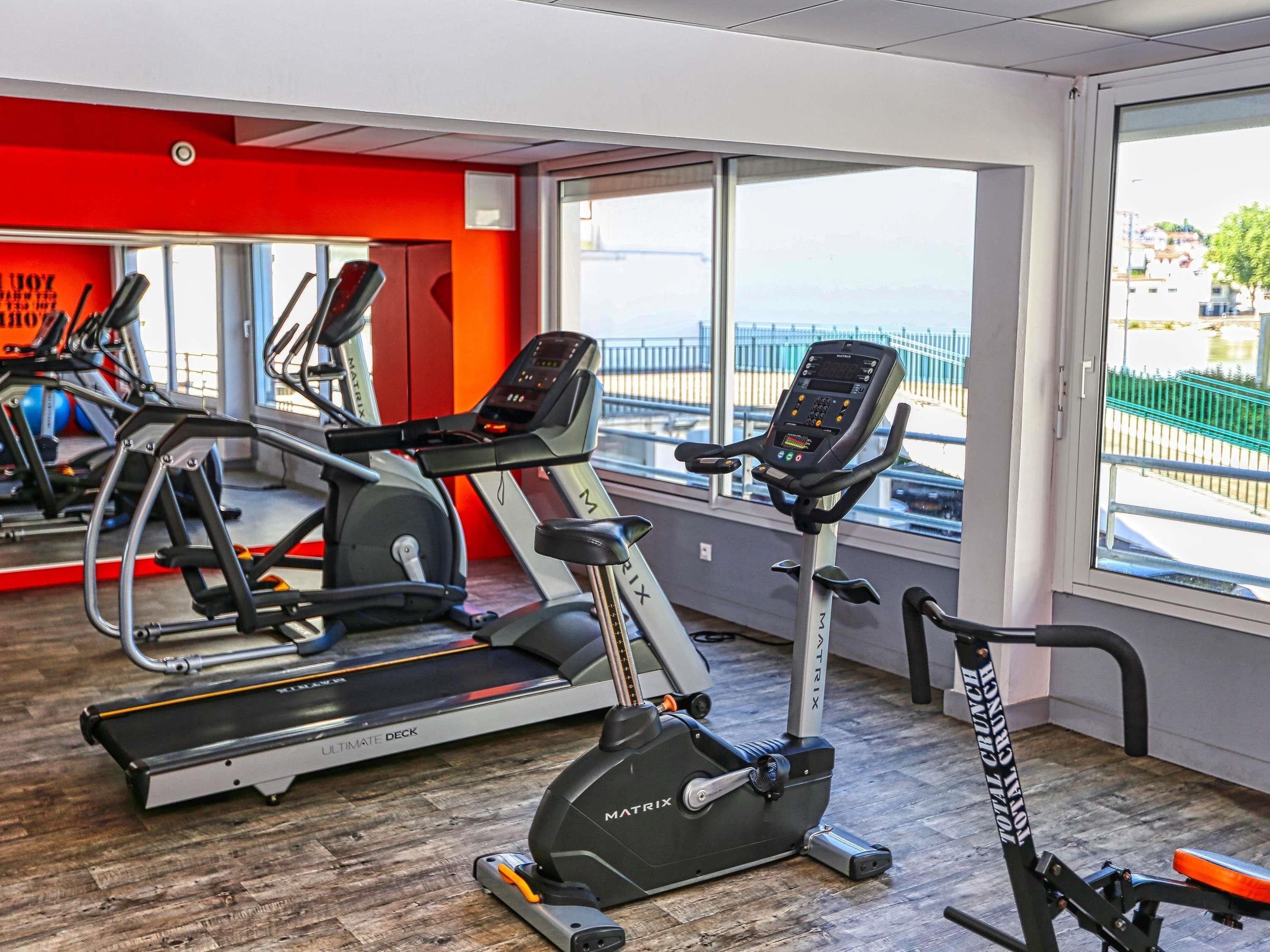 Een fitnessruimte met cardioapparaten, een spiegelwand en grote ramen.