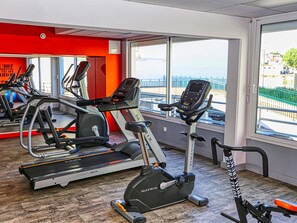 A gym with cardio machines, a mirrored wall, and large windows.