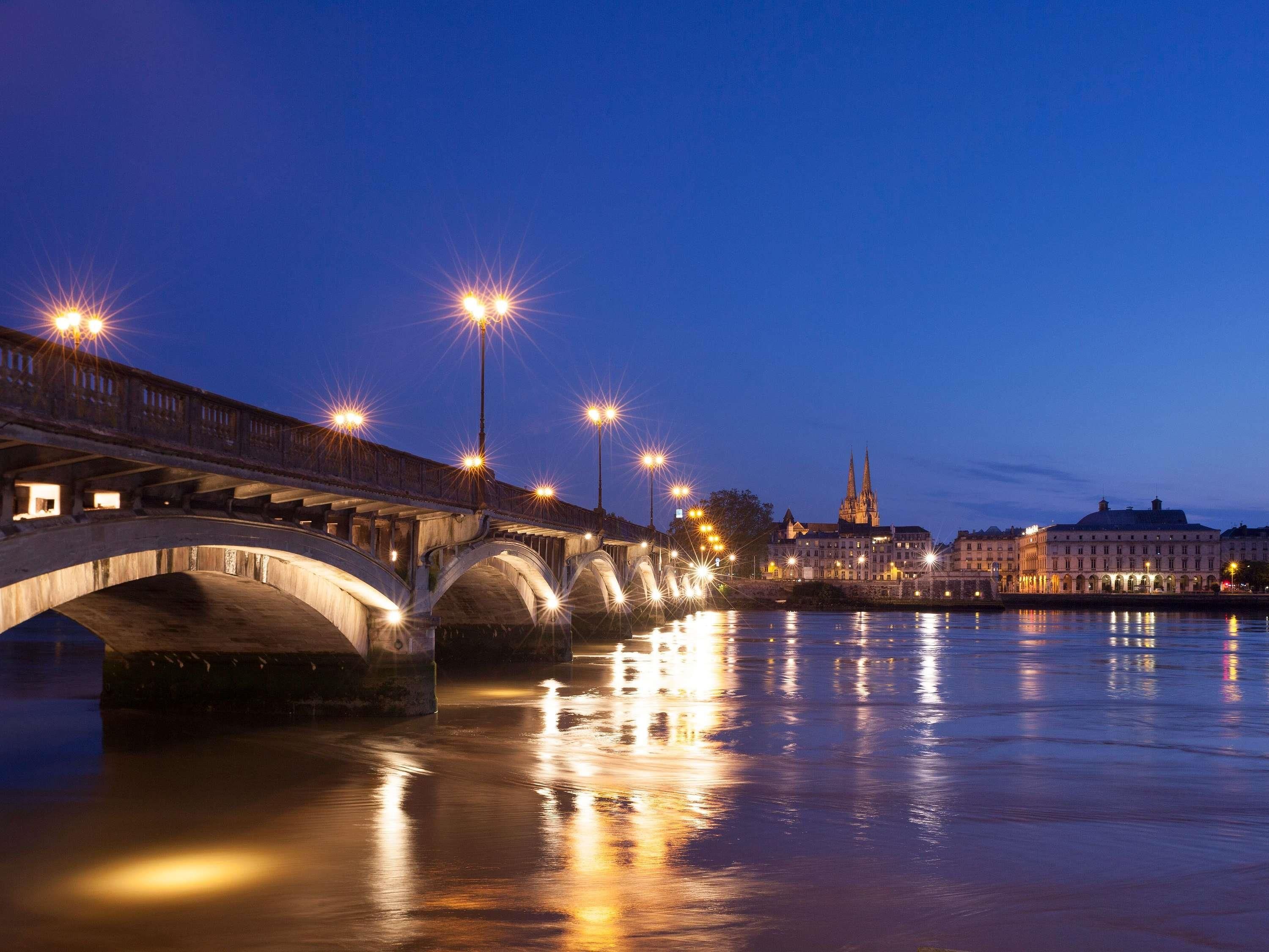 Un pont à arches multiples enjambant une étendue d’eau, dont les lumières se reflètent à la surface.