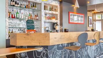A bar area with shelves of bottles and glasses, a wooden counter, and bar stools.