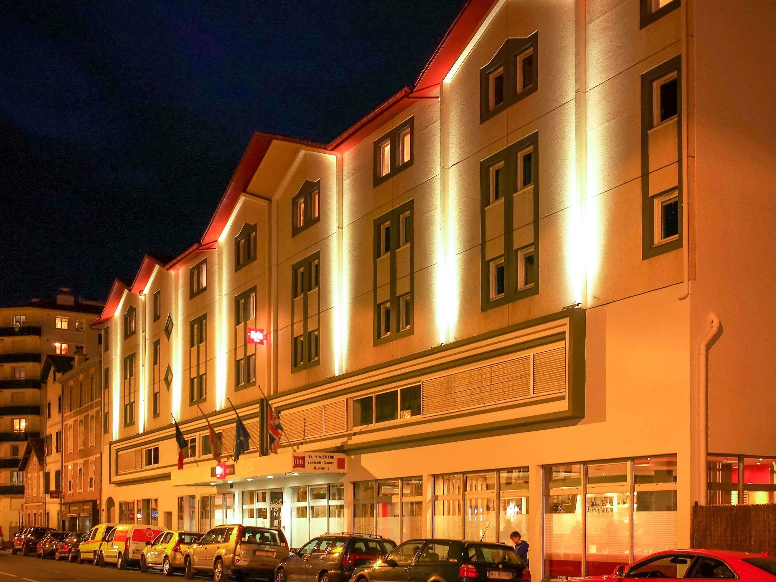 Un hôtel à plusieurs étages, avec une rangée de voitures garées devant.