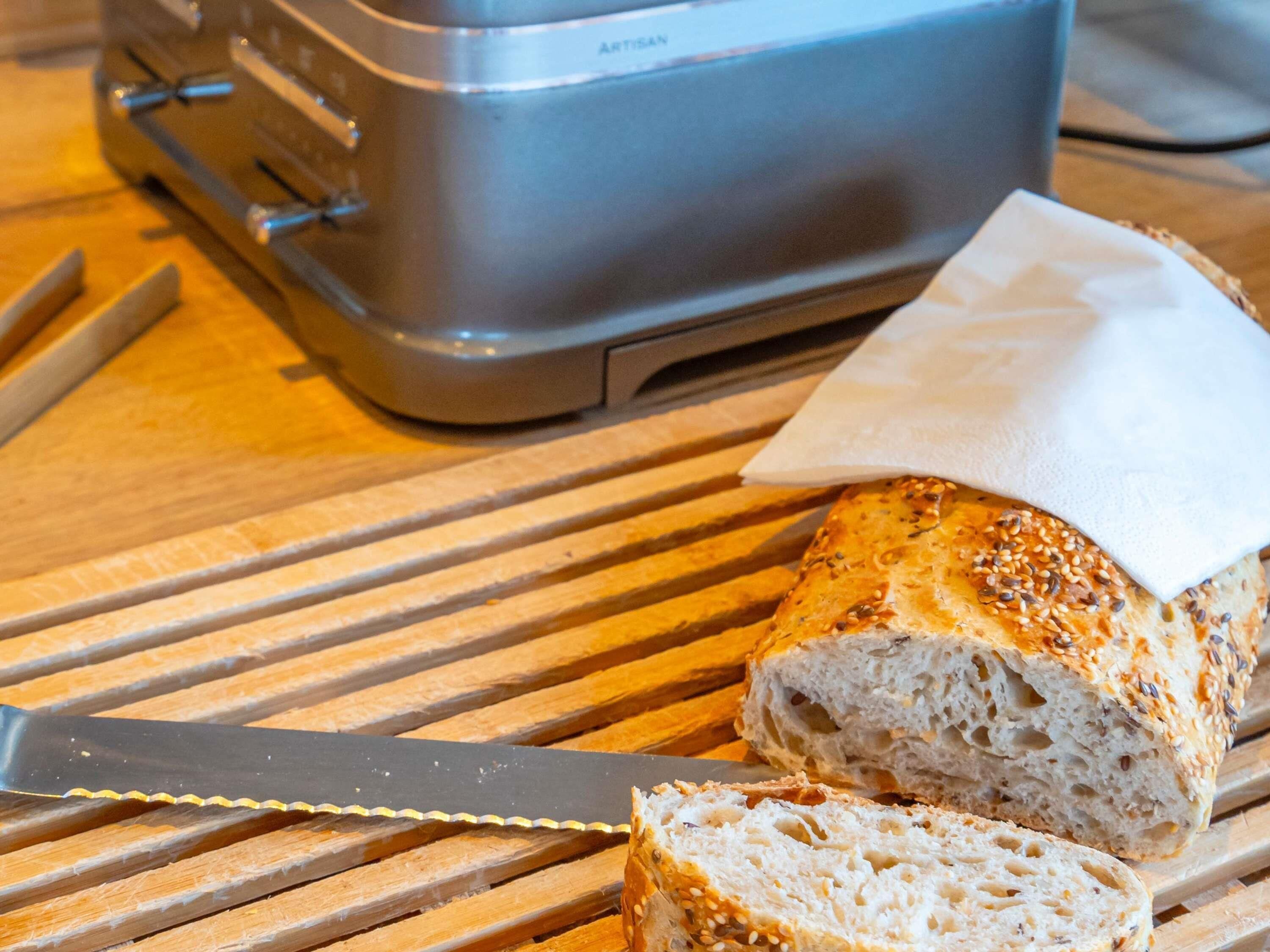 Brød med sesamfrø på en træ skærebræt, en kniv og en brødrister.