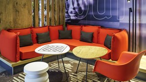 A modern lounge area with a red sofa, two round tables, and a single orange chair.