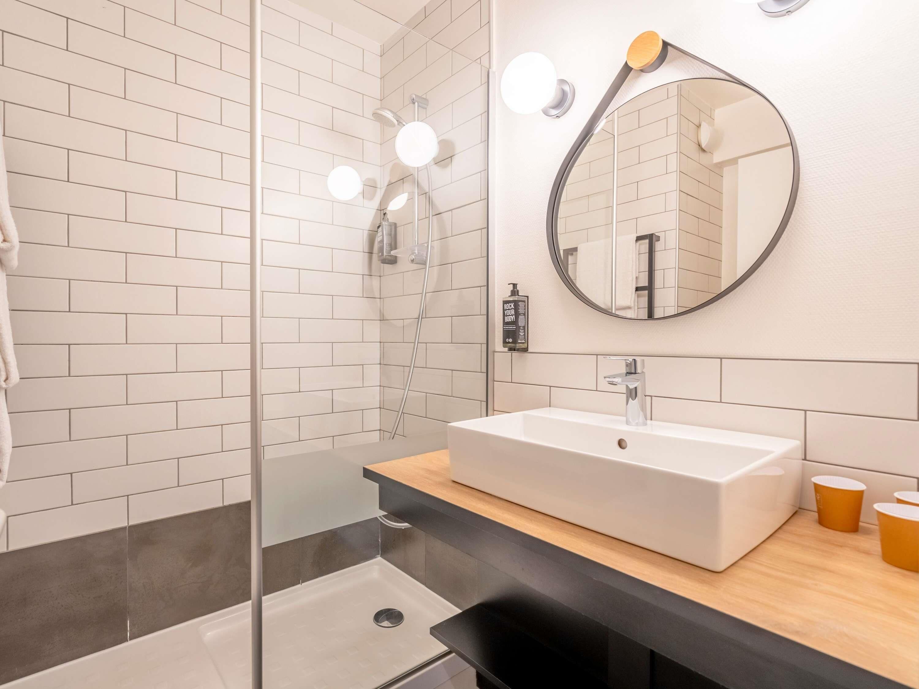 A modern bathroom with a glass shower enclosure, a white sink, a round mirror, and a wooden countertop.