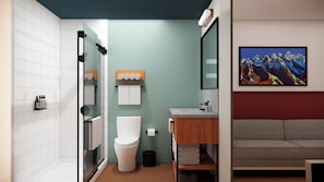 A modern bathroom with a glass shower enclosure, a toilet, a sink with a wooden vanity, and a painting of mountains on the wall.