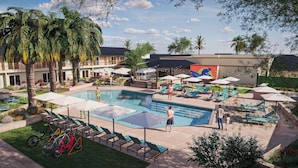 A pool area with lounge chairs and umbrellas, surrounded by palm trees and a building with a mural. - LOGE St. George (St. George)
