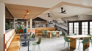 A modern cafe with wooden ceiling beams, green chairs, and a mural of mountains on the wall. - LOGE St. George (St. George)