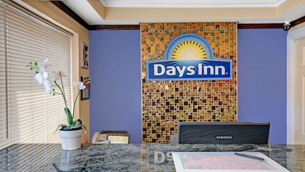 A reception desk with a Days Inn sign, a Samsung phone, and a potted orchid. - Days Inn by Wyndham San Francisco - Lombard (San Francisco)