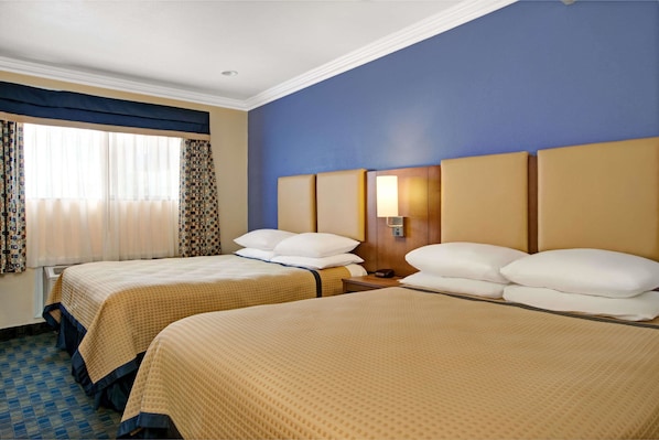 A hotel room with two beds, a window with curtains, a nightstand with a lamp, and a blue accent wall.