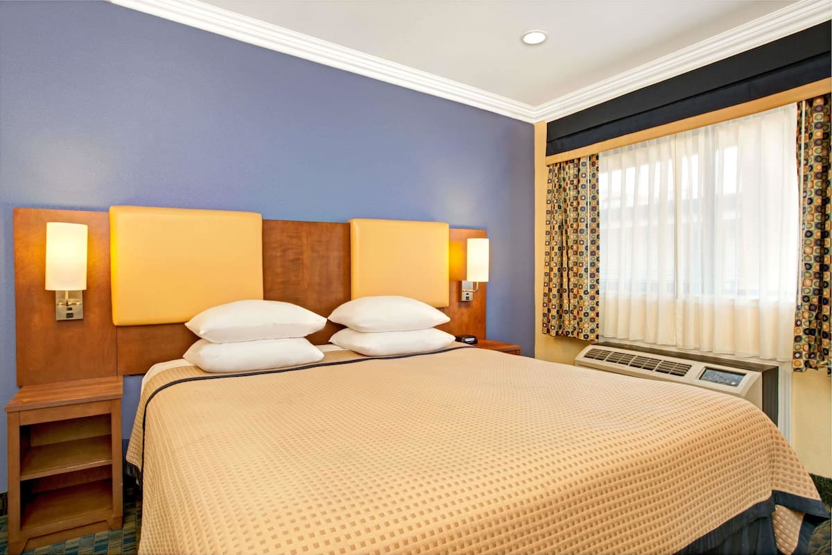 Une chambre d’hôtel avec un grand lit, deux lampes de chevet, une fenêtre avec des rideaux à motifs et un climatiseur fixé au mur.