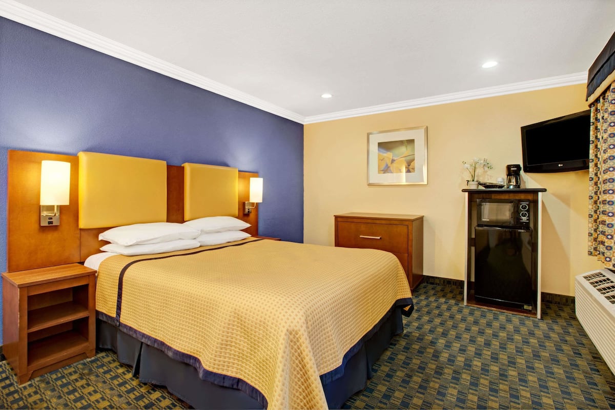 Une chambre d’hôtel comprenant un lit, des tables de chevet, un bureau avec une machine à café, un four à micro-ondes et une télévision.