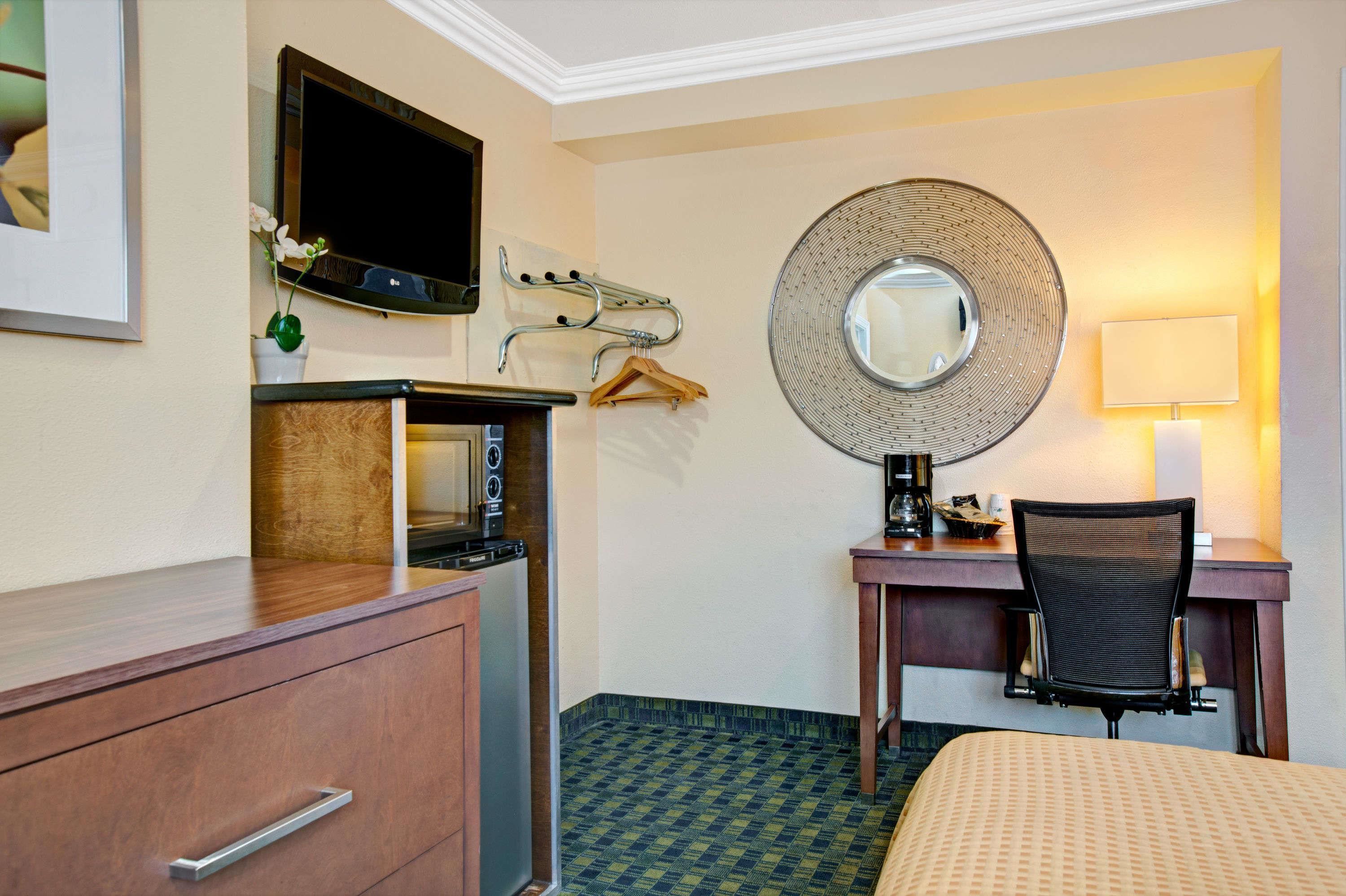 Een hotelkamer met een bed, een bureau met stoel, een televisie, een spiegel, een kapstok en een dressoir.