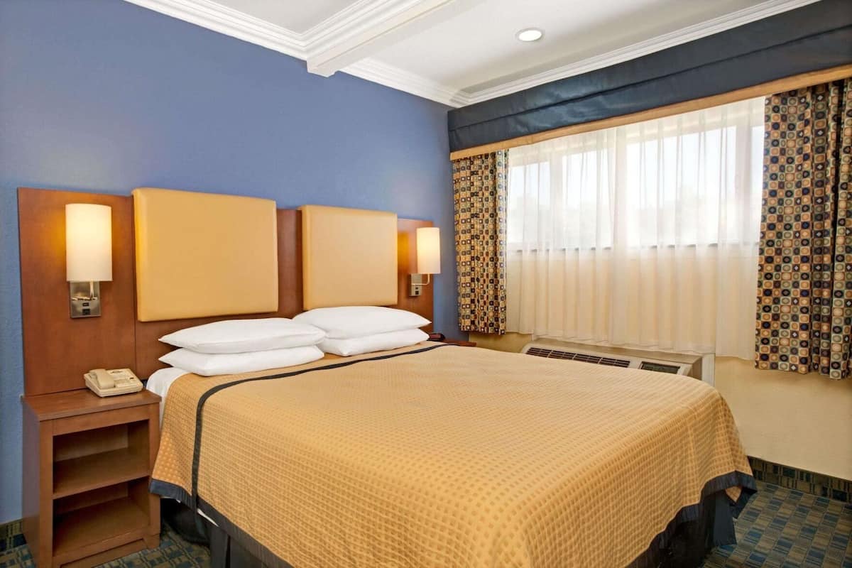 Une chambre d’hôtel avec un grand lit, deux lampes de chevet, un téléphone et une fenêtre avec des rideaux à motifs.
