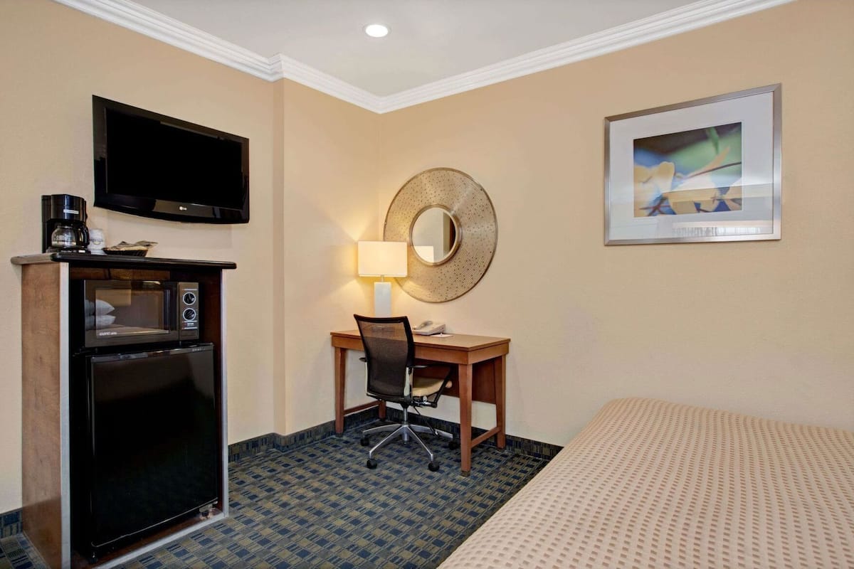 Une chambre d’hôtel équipée d’un téléviseur à écran plat, d’une machine à café, d’un four à micro-ondes, d’un bureau avec une chaise, d’une table de chevet, d’une lampe, d’un lit et d’un tableau encadré au mur.