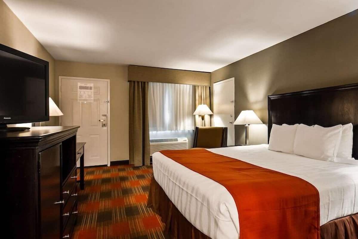 Una camera d'hotel con un letto, televisione, una scrivania e una finestra con tende.