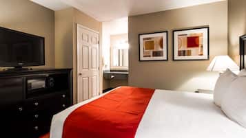 A hotel room with a bed, a television, a dresser, a bathroom, and two framed pictures on the wall.