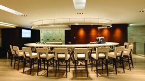 A modern dining area with a round table surrounded by chairs, a bar area, and a projection screen in the background. - Prudential Hotel (Kowloon)