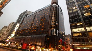 A modern building with a curved glass facade, multiple floors, and a prominent cylindrical structure on top. - Prudential Hotel (Kowloon)