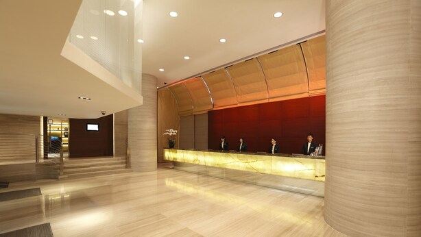 A modern hotel lobby with a reception desk, a staircase, and a large column. - Prudential Hotel (Kowloon)