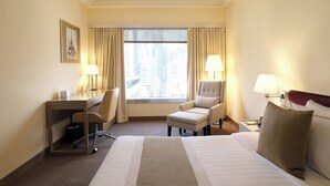 A hotel room with a large bed, a desk with a chair, a small armchair, and a window with curtains. - Prudential Hotel (Kowloon)