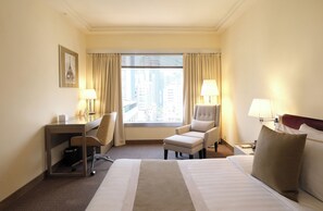 A hotel room with a large bed, a desk with a chair, a small armchair, and a window with curtains. - Prudential Hotel (Kowloon)