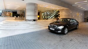 A modern hotel entrance with a black car parked in front, a staircase leading to the lobby, and a large pillar. - Prudential Hotel (Kowloon)