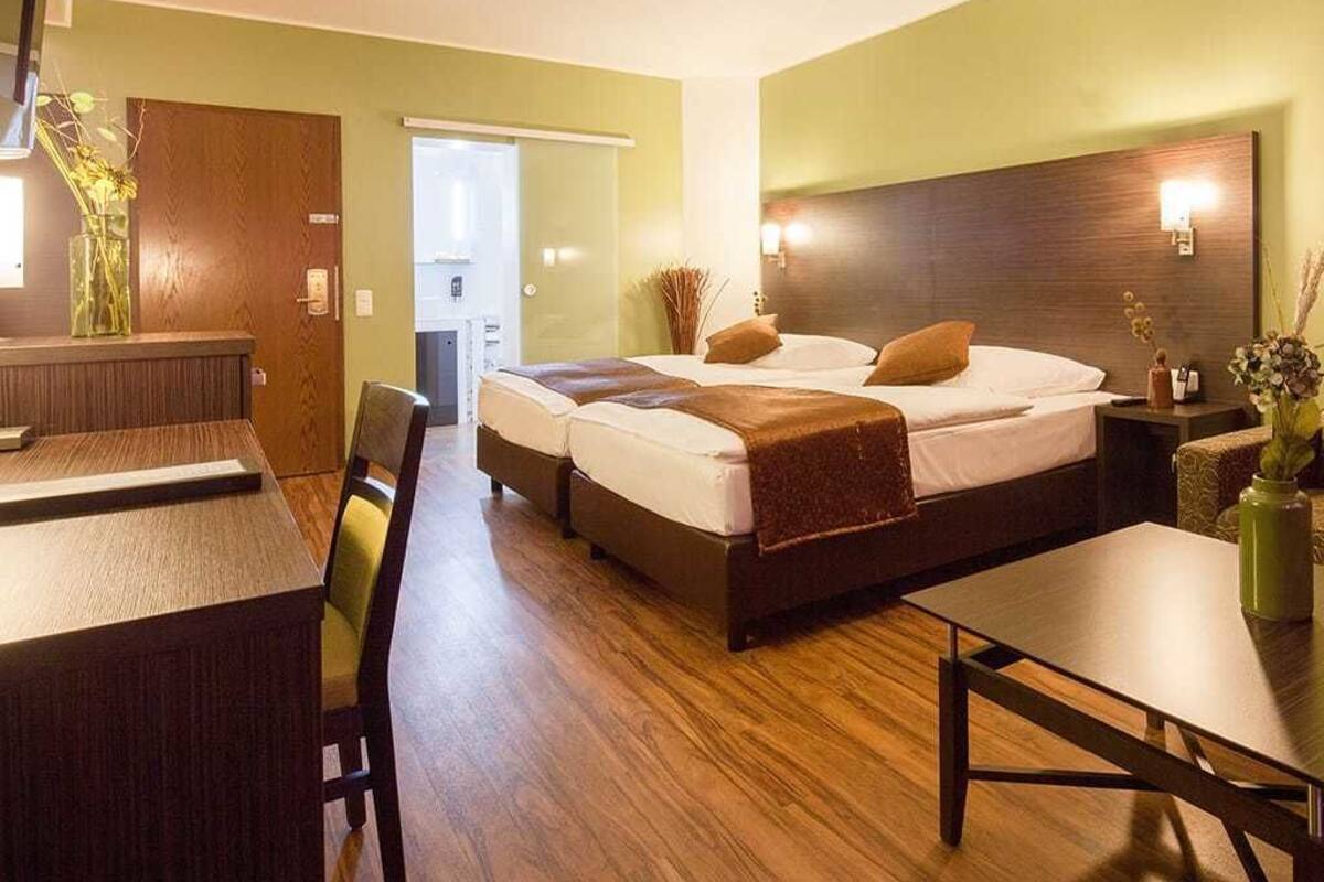 A hotel room with a bed, bedside tables, a desk, and a chair.