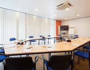A conference room with a long table, blue chairs, and a television screen. - Hotel Mondial (Langenfeld)