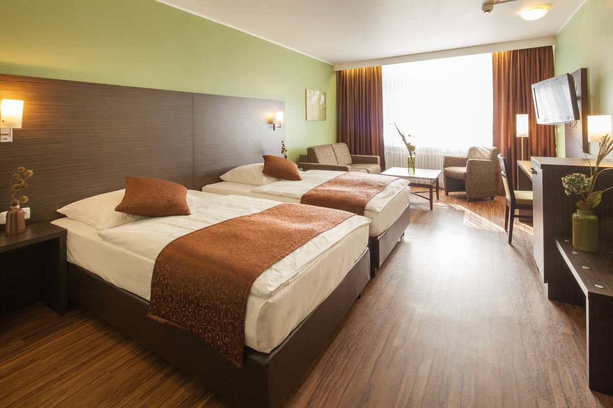 A hotel room with two beds, a sofa, a TV, and a desk.