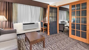 A hotel room with a sofa, a small table, a desk, and a large window with curtains.
