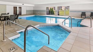 An indoor swimming pool with a tiled floor, a pool table, and a seating area with chairs.