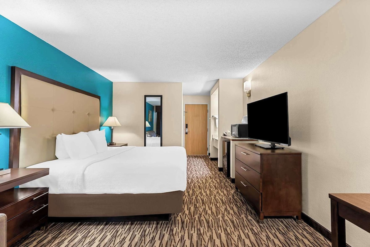 A hotel room with a bed, bedside tables, a TV, a mirror, and a carpeted floor.