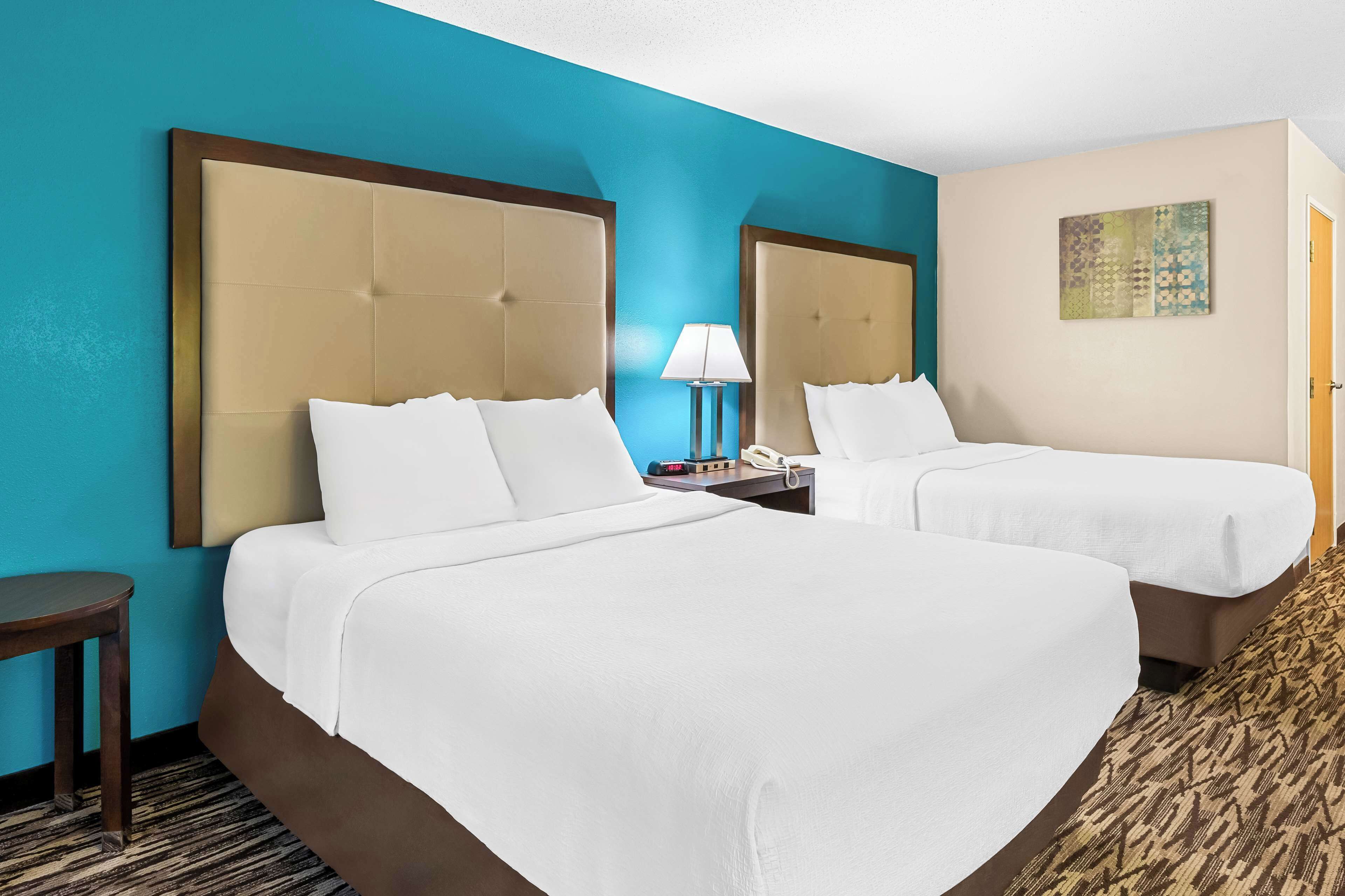 Habitación de hotel con dos camas, una mesita de noche con lámpara y un cuadro en la pared.
