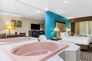 A hotel room with a large pink bathtub, a bed, a desk with a lamp, a television, and a window with curtains. - Best Western Baraboo Inn (Baraboo)