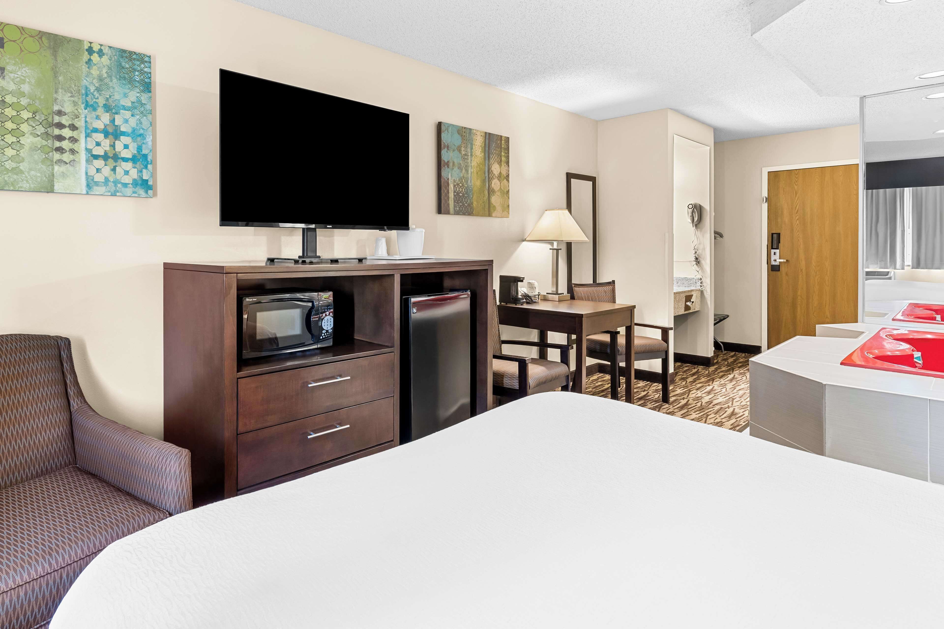 A hotel room with a bed, a TV, a desk, a chair, a lamp, and a bathroom with a red sink.
