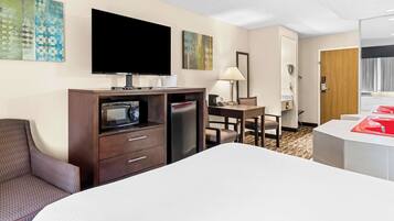 A hotel room with a bed, a TV, a desk, a chair, a lamp, and a bathroom with a red sink.