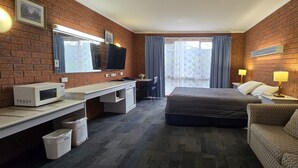 A hotel room with a brick wall, a bed, a desk with a computer, a TV, and a couch.