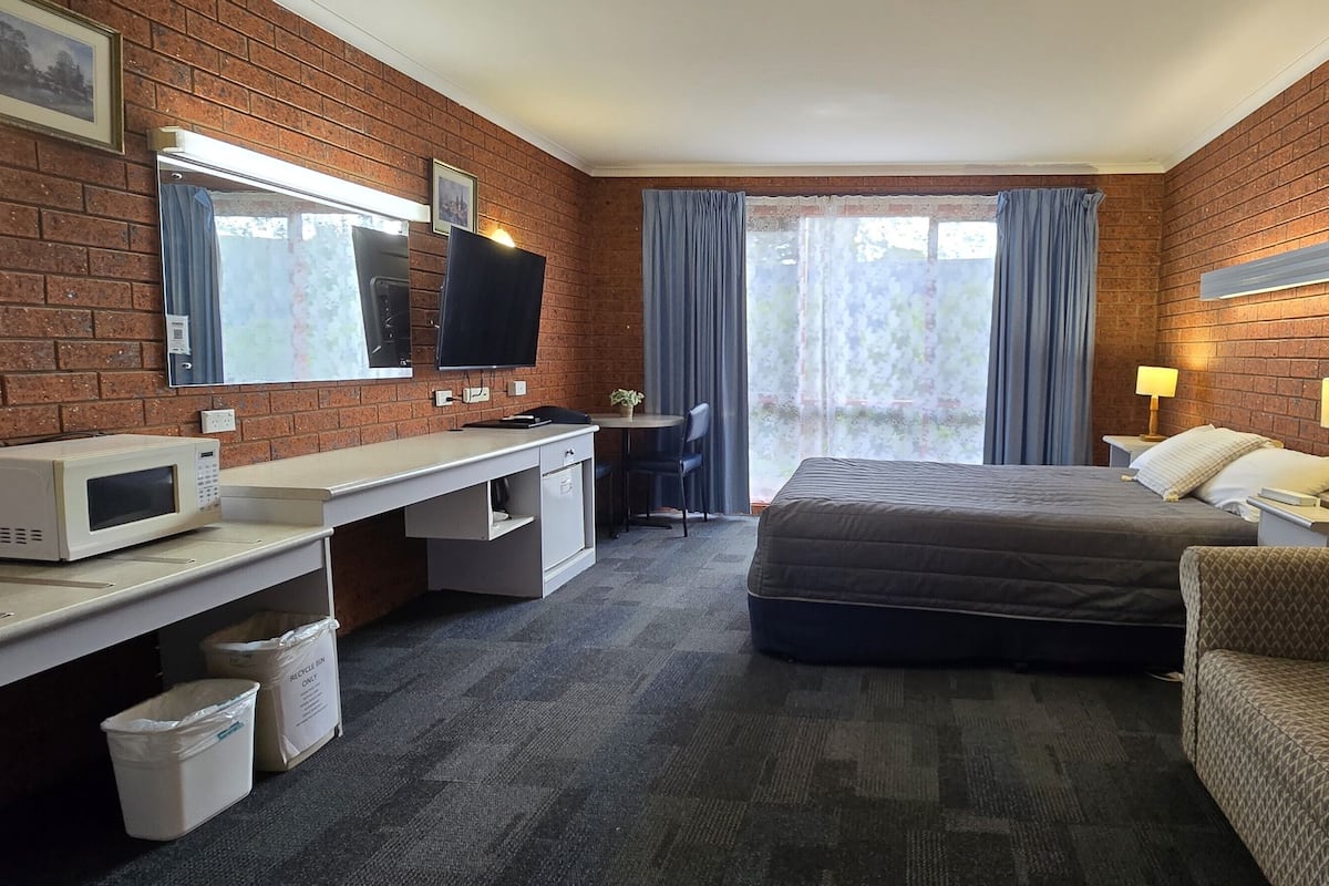 A hotel room with a brick wall, a bed, a desk with a computer, a TV, and a couch.