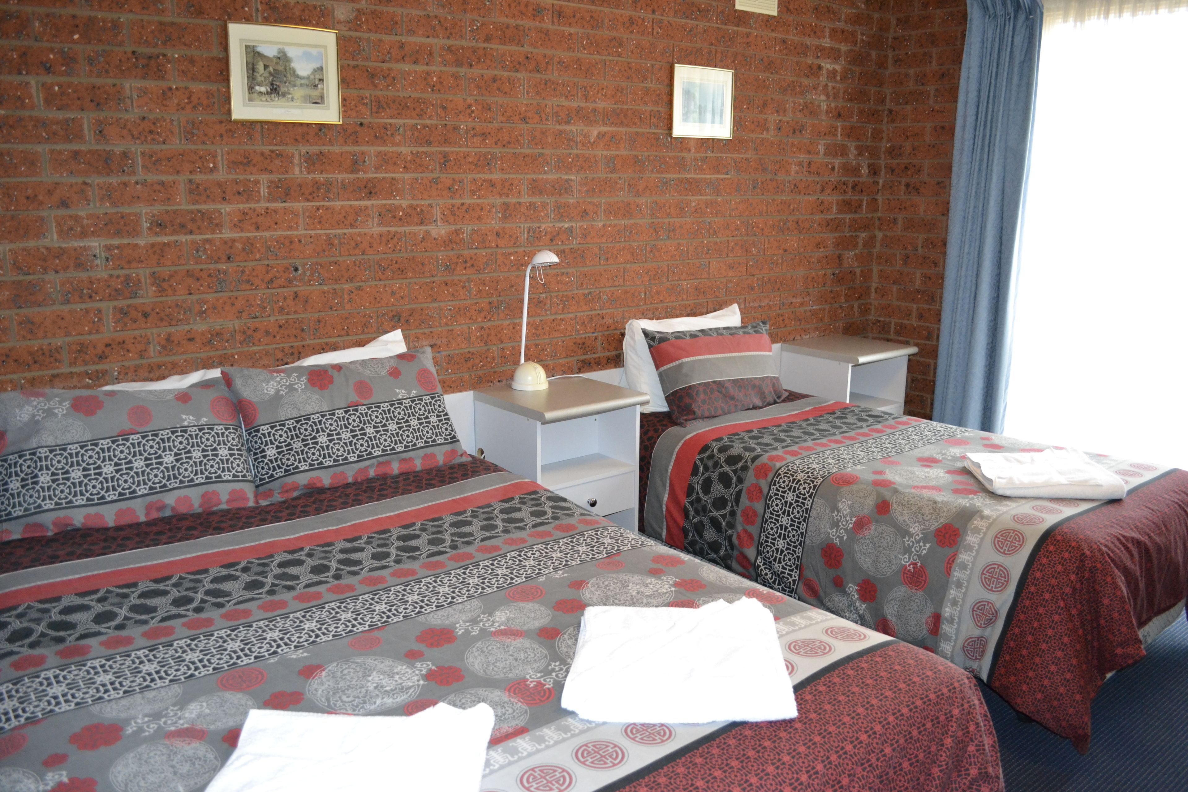 A room with two beds, a nightstand, a lamp, and a brick wall.