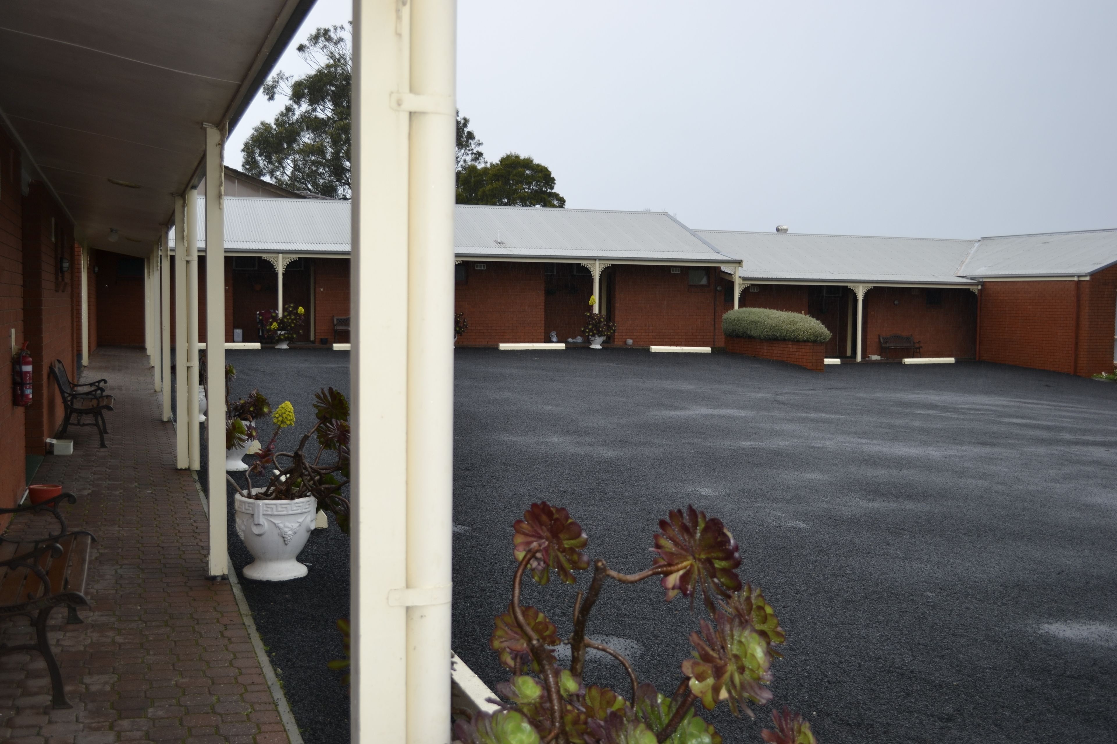 A covered outdoor area with multiple rooms, potted plants, and a paved walkway.