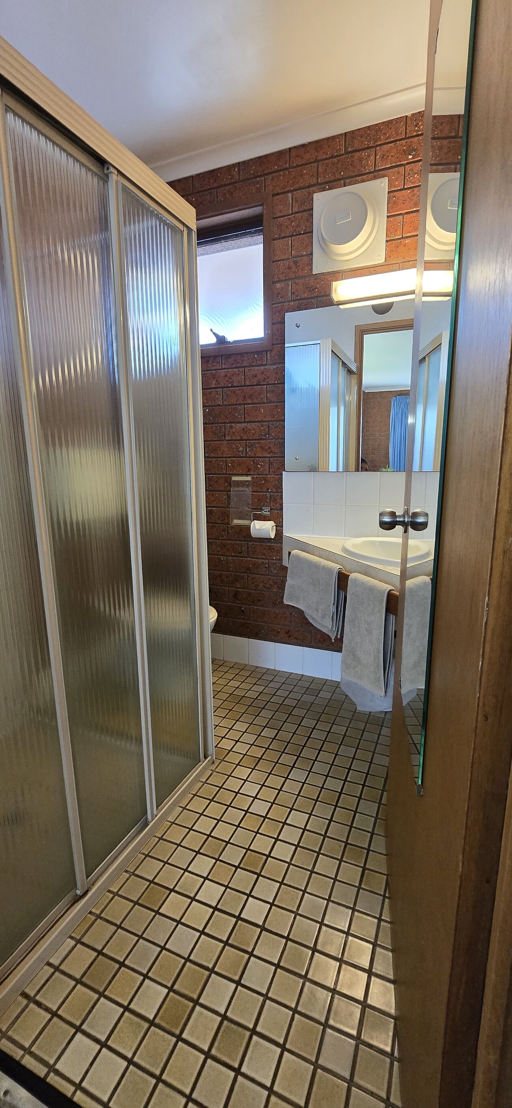 A bathroom with a tiled floor, a toilet, a sink with a mirror, and a towel rack.