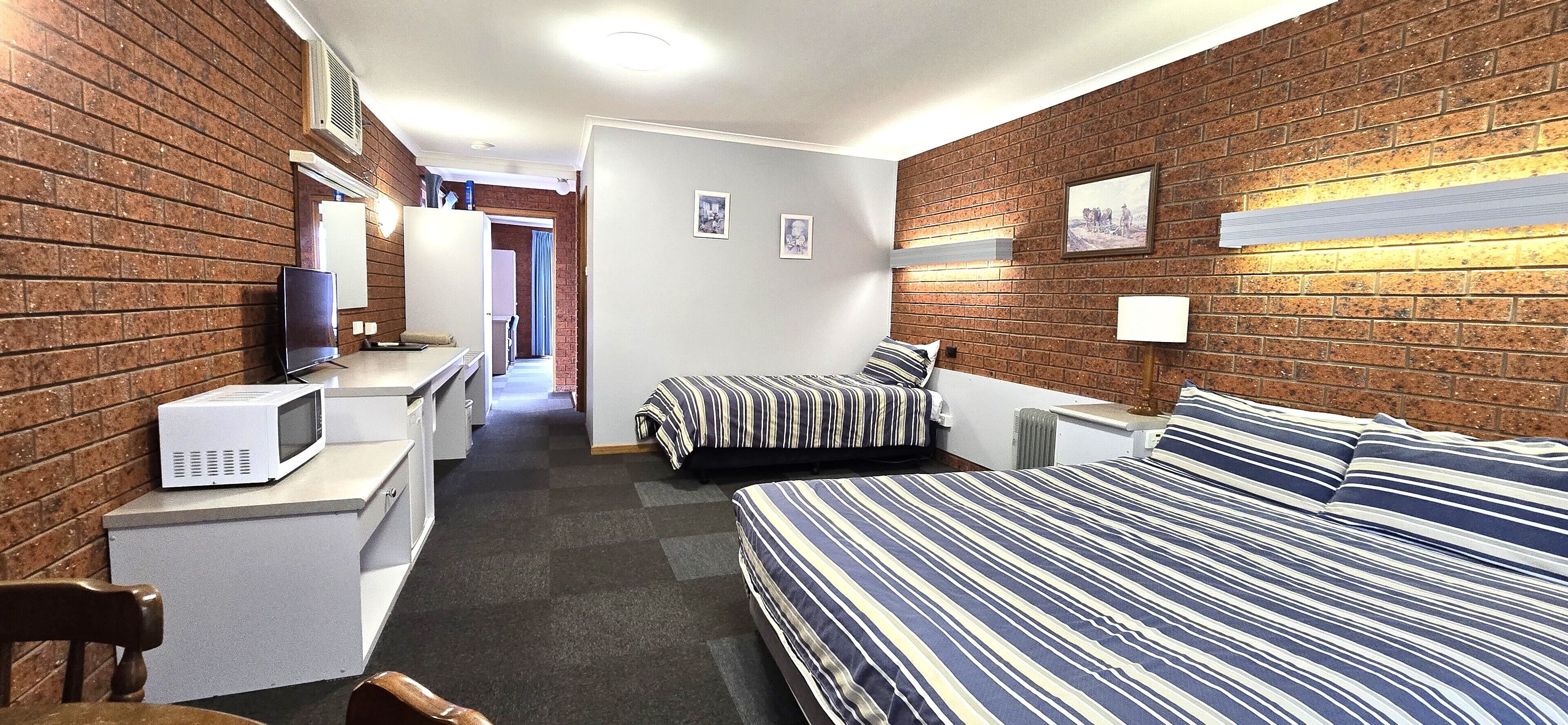 A hotel room with a brick wall, a bed with striped bedding, a microwave, a desk, and a chair.