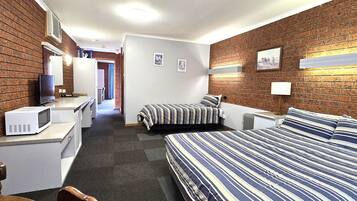 A hotel room with a brick wall, a bed with striped bedding, a microwave, a desk, and a chair.