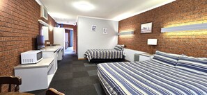 A hotel room with a brick wall, a bed with striped bedding, a microwave, a desk, and a chair.